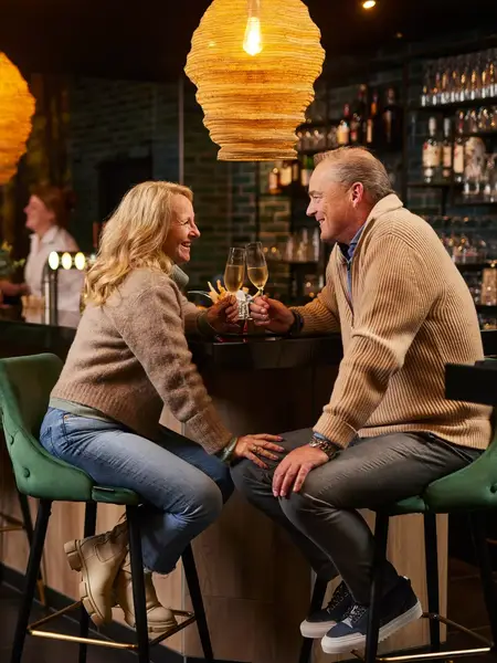 A couple toasts with champagne in an atmospheric bar.