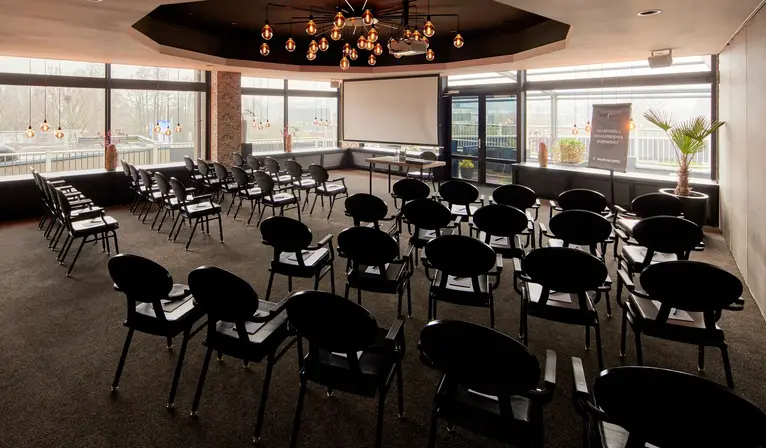 Salle de réunion Toucan aménagée en salle de spectacle avec écran de projection et bénéficiant d'une abondante lumière naturelle à l'hôtel Van der Valk de Leusden-Amersfoort