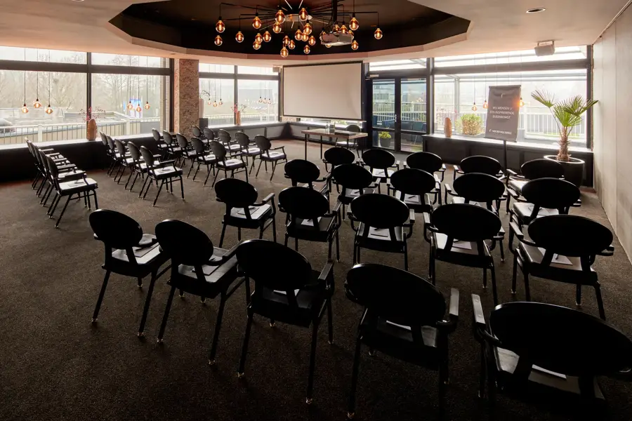 Salle de réunion Toucan aménagée en salle de spectacle avec écran de projection et bénéficiant d'une abondante lumière naturelle à l'hôtel Van der Valk de Leusden-Amersfoort