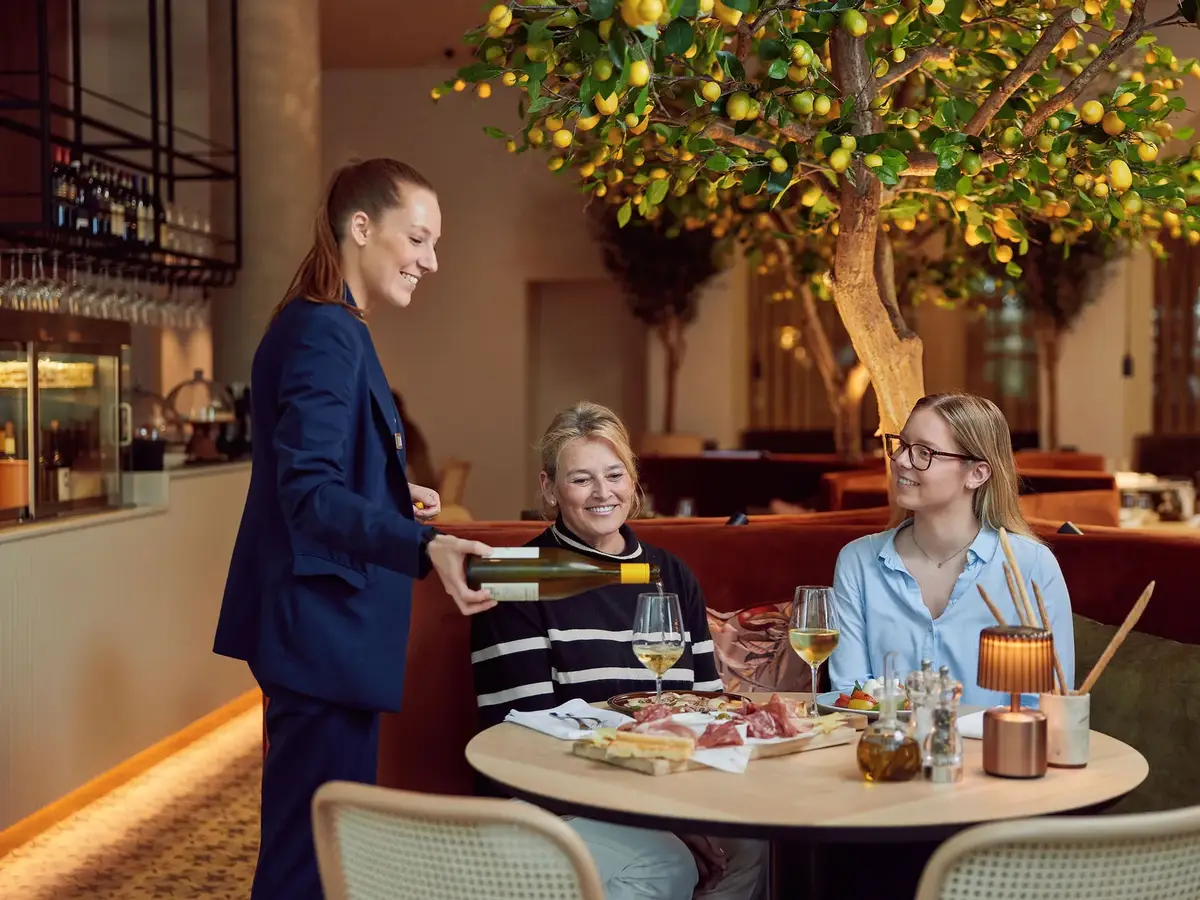 Medewerker van een restaurant schenkt wijn in bij twee dames aan tafel.
