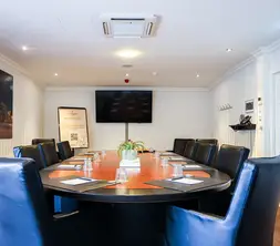 Overzicht van een lichte boardroom met een ruime ovale vergadertafel, comfortabele stoelen en een presentatiescherm.