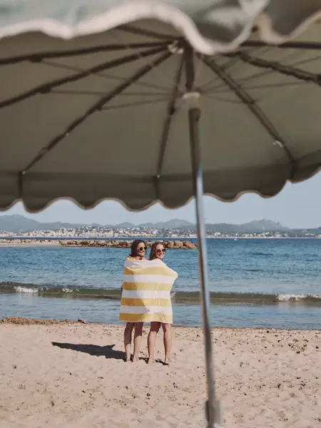 2 meiden omwikkeld in een handdoek aan zee, gezien vanonder een parasol