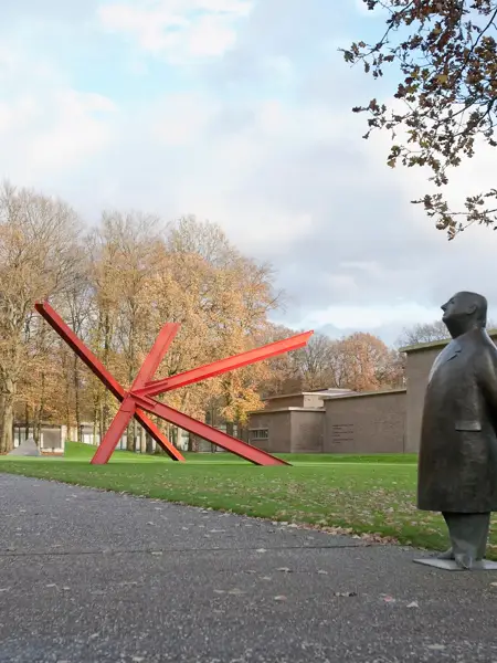 Exterior view of the Kröller-Müller Museum with red artwork and statue.