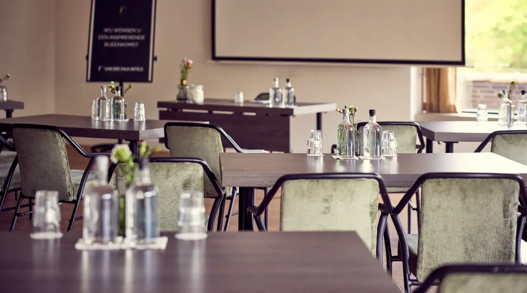 Saal im Hotel Arnhem. Saal ist in der Kabarettbestuhlung. Grüne Stühle mit schwarzen Rändern. Dunkelbraune Tische.