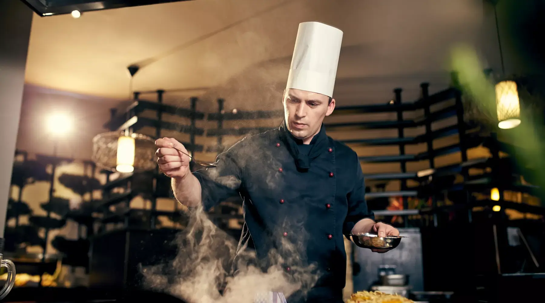 Chefkoch bereitet ein Gericht in der Küche zu, während Dampf aus der Pfanne aufsteigt.