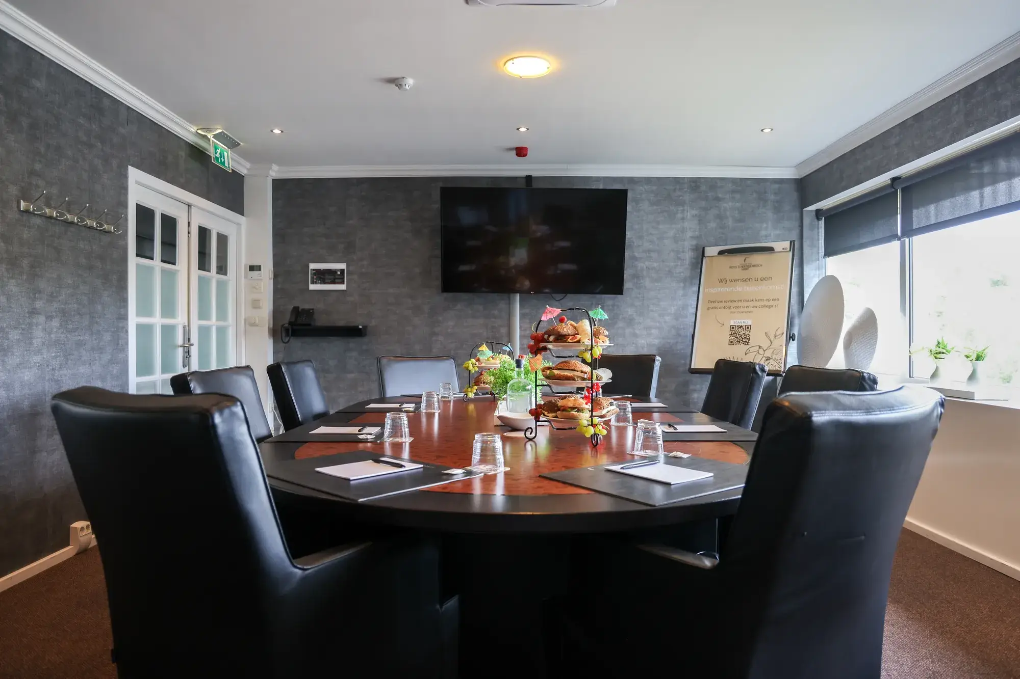 Sfeervolle boardroom met een grote ovale vergadertafel voor maximaal 10 personen, zwarte stoelen en een LCD-scherm aan de wand.