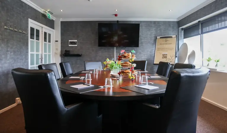 Sfeervolle boardroom met een grote ovale vergadertafel voor maximaal 10 personen, zwarte stoelen en een LCD-scherm aan de wand.