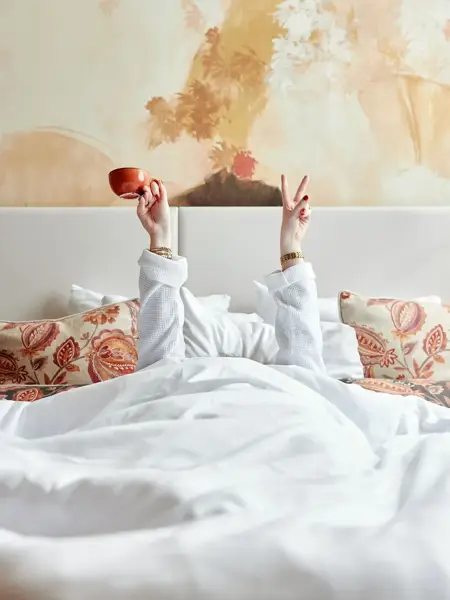 Woman in bed raising her hands from under the covers
