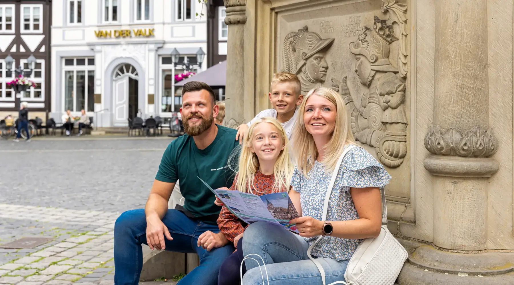Een familie zit op het marktplein bij de fontein. Op de achtergrond is het Van der Valk te zien. Ze lezen een stadsplattegrond. Foto: Christian Bierwagen