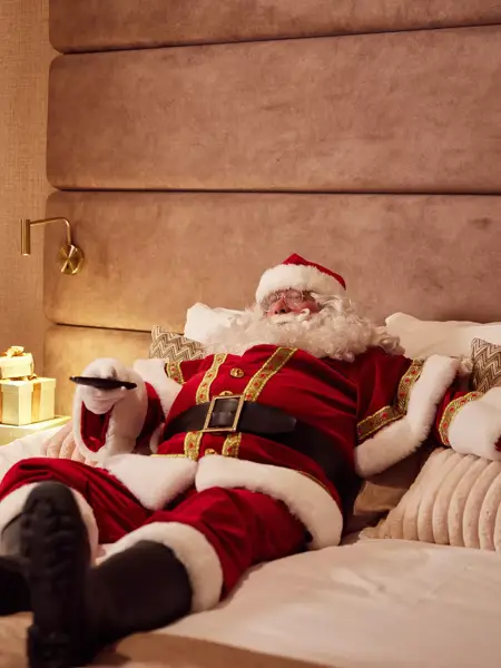 Santa Claus in bed with a remote control.