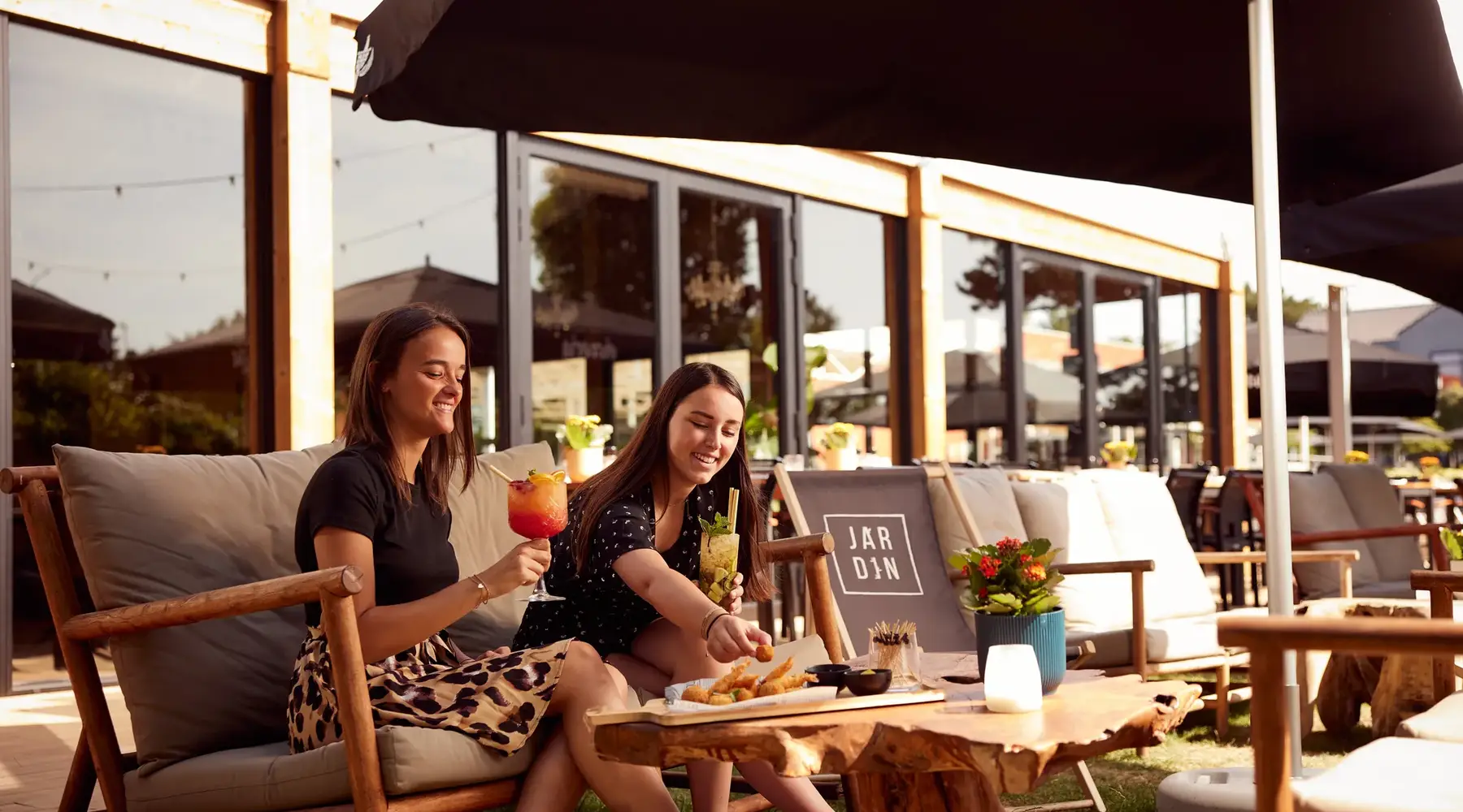 2 Mädchen mit einem Cocktail und einer Snackplatte auf einer Sommerterrasse eines Hotels