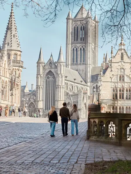 Mensen lopen in het centrum van Gent, met op de achtergrond een grote kerk