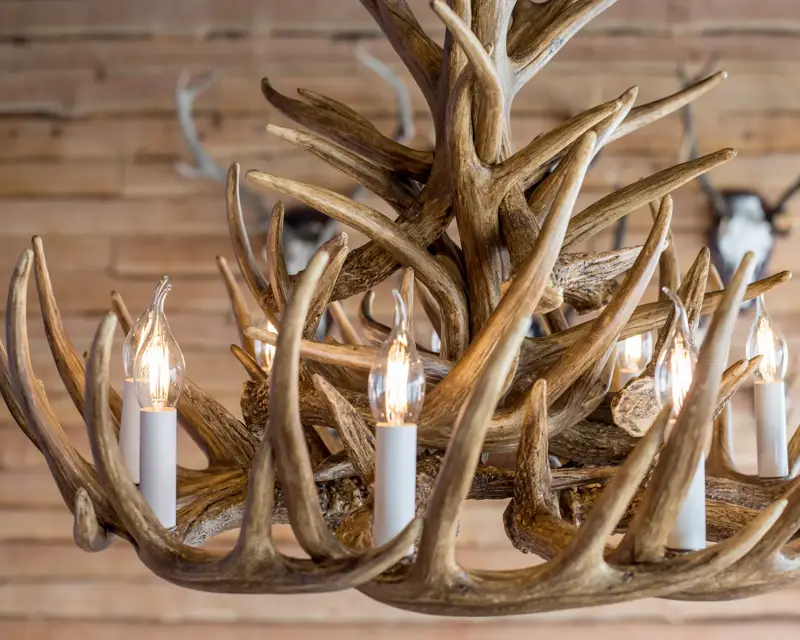Een decoratieve kroonluchter gemaakt van houten geweien met kaarsvormige lampen, passend bij de chaletstijl.
