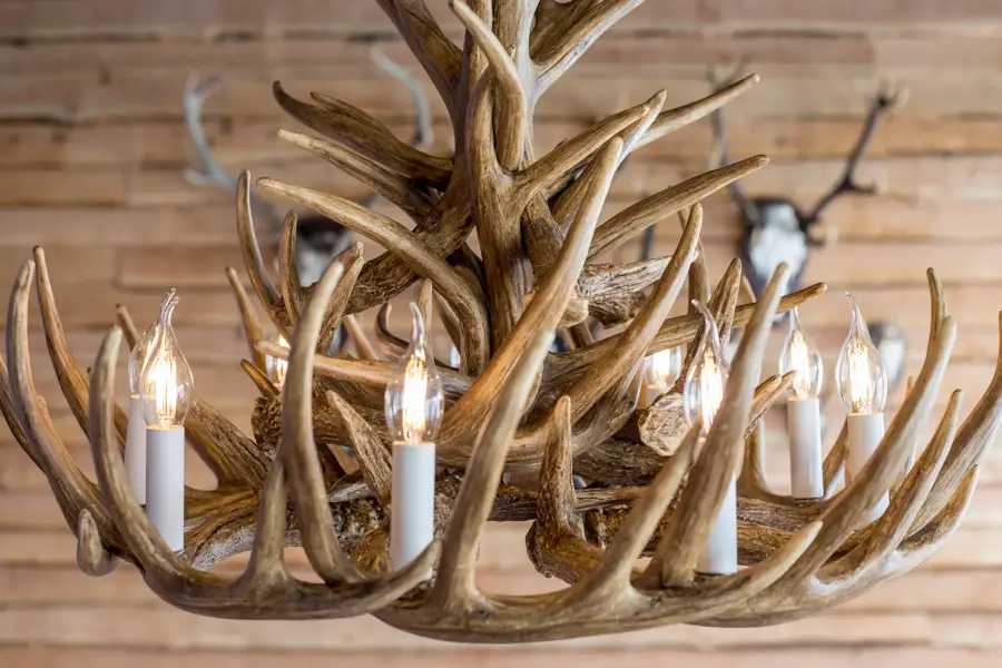 Een decoratieve kroonluchter gemaakt van houten geweien met kaarsvormige lampen, passend bij de chaletstijl.