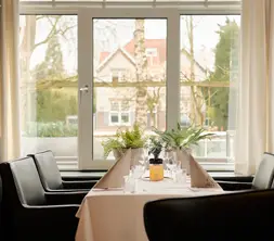 Stylishly set dining table in Zaal de Witte, situated directly by the window with natural daylight and a view to the outside.