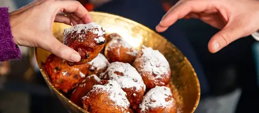 Die Leute nehmen Oliebollen aus einer Schüssel.