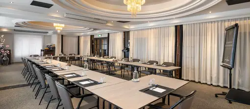 Brede blik op de vergaderzaal met een royale U-opstelling, opvallende plafondverlichting en de aanwezige vergaderfaciliteiten.