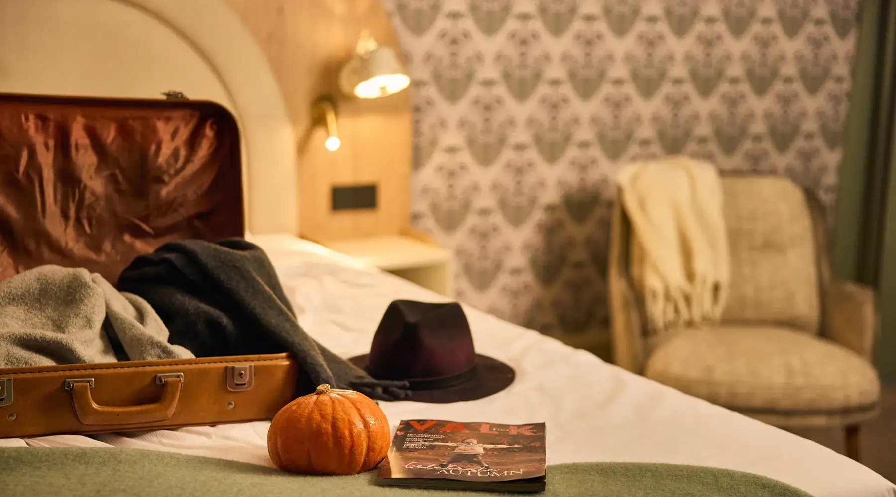 Autumn stay in a hotel. Suitcase and small pumpkin are on the bed.