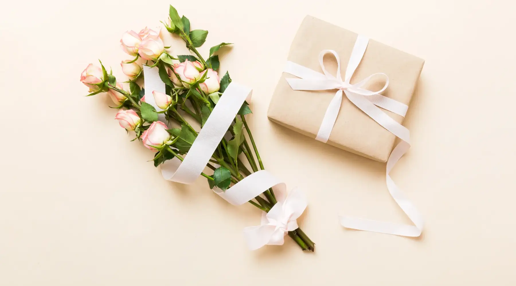 Ein Strauß zarter Rosen liegt neben einer in Papier verpackten Geschenkbox mit Schleife auf einer hellen Oberfläche im Van der Valk Hotel Hildesheim. Die sanften Farben und die minimalistische Anordnung erzeugen eine elegante, ruhige Stimmung, passend für besondere Anlässe wie Feiern oder Hochzeiten.