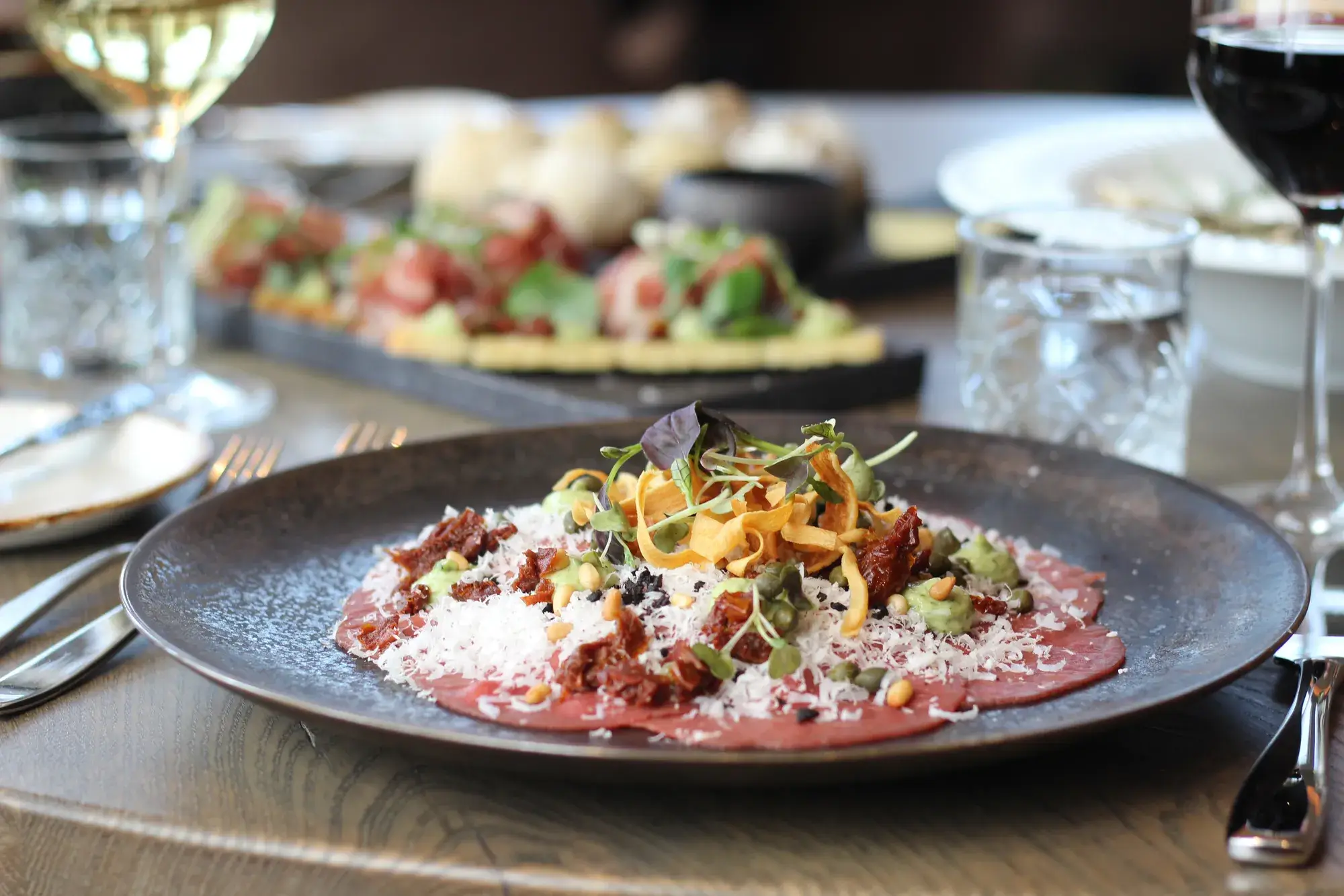 Geräuchertes Rindercarpaccio auf einem Tisch im Restaurant Vloed, serviert mit Wein