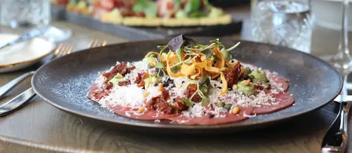 Geräuchertes Rindercarpaccio auf einem Tisch im Restaurant Vloed, serviert mit Wein
