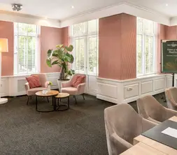 Deel van de vergaderzaal met zicht op de vele raampartijen en een informele zithoek met twee stoelen.