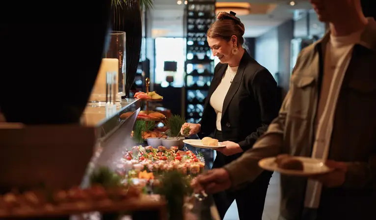 Zwei Personen bedienen die Gäste an einem Buffet.