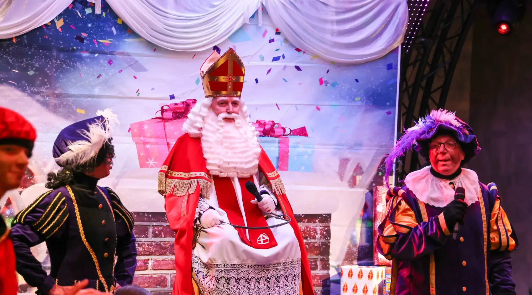 Saint-Nicolas est assis sur sa chaise avec des lutins autour de lui 