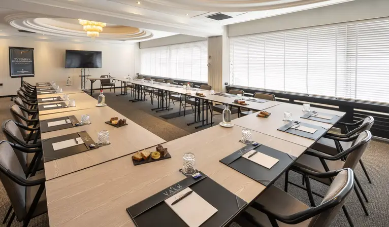Overzicht van de moderne Strausszaal in een ruime U-opstelling, voorzien van veel daglicht en een LCD-scherm voor presentaties.
