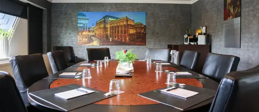 Brede blik op de boardroom met een centraal geplaatste ovale tafel, opgemaakte werkplekken en een wanddecoratie op de achtergrond.