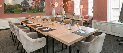 Brede blik op de sfeervolle zaal met de centrale vergadertafel, opvallende roze wanden en een grote fotodecoratie aan de muur.
