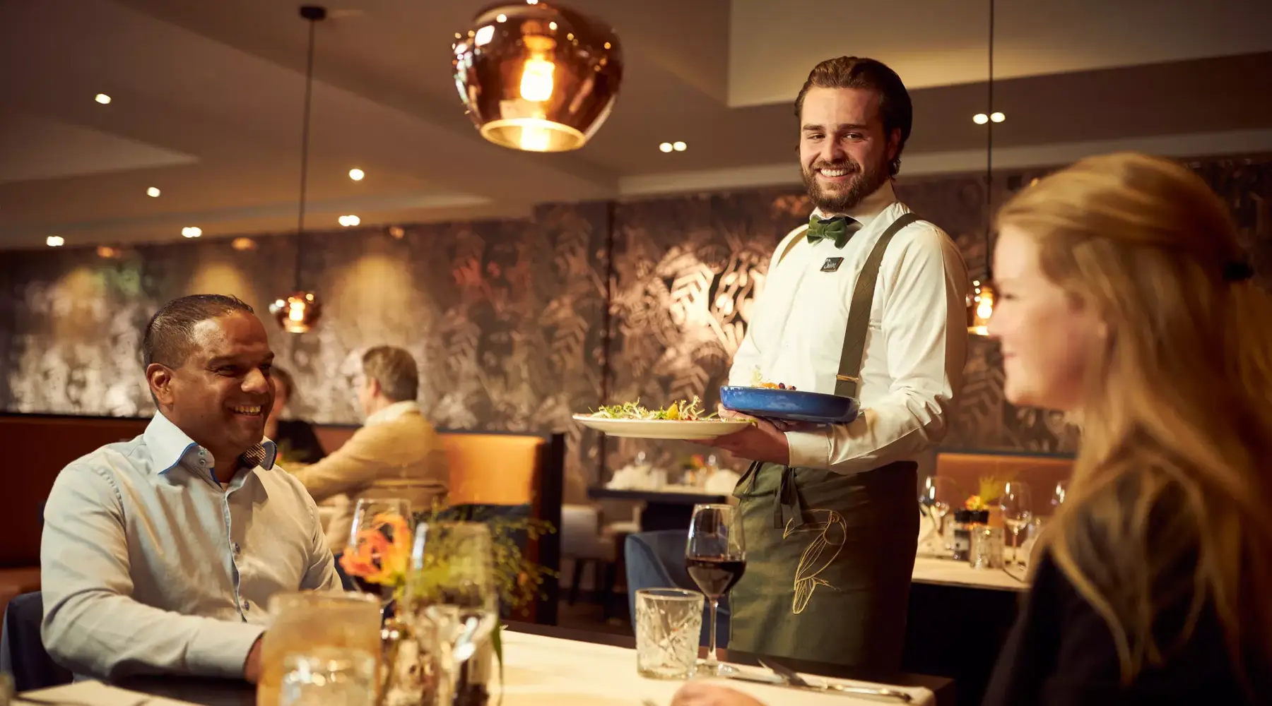 Ober serveert eten bij stel aan de tafel.