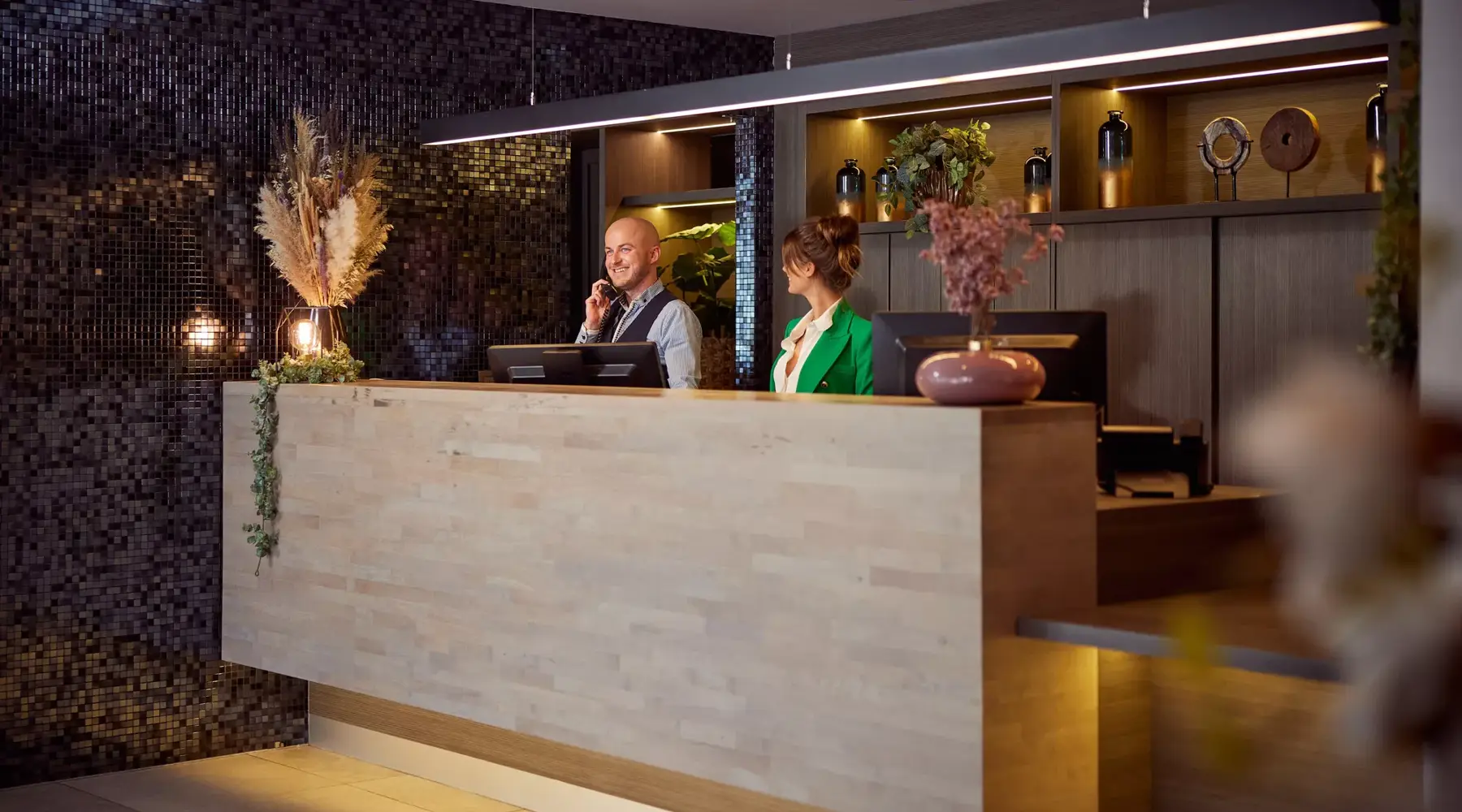 Receptie hotel Dennenhof. 2 personen achter de balie. een man en een vrouw.