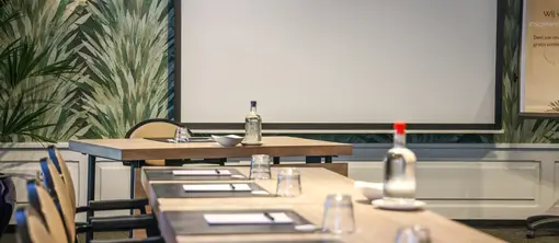 Detail of the set meeting tables in room De IJzeren Man, provided with stationery and water, with the projection screen in the background.