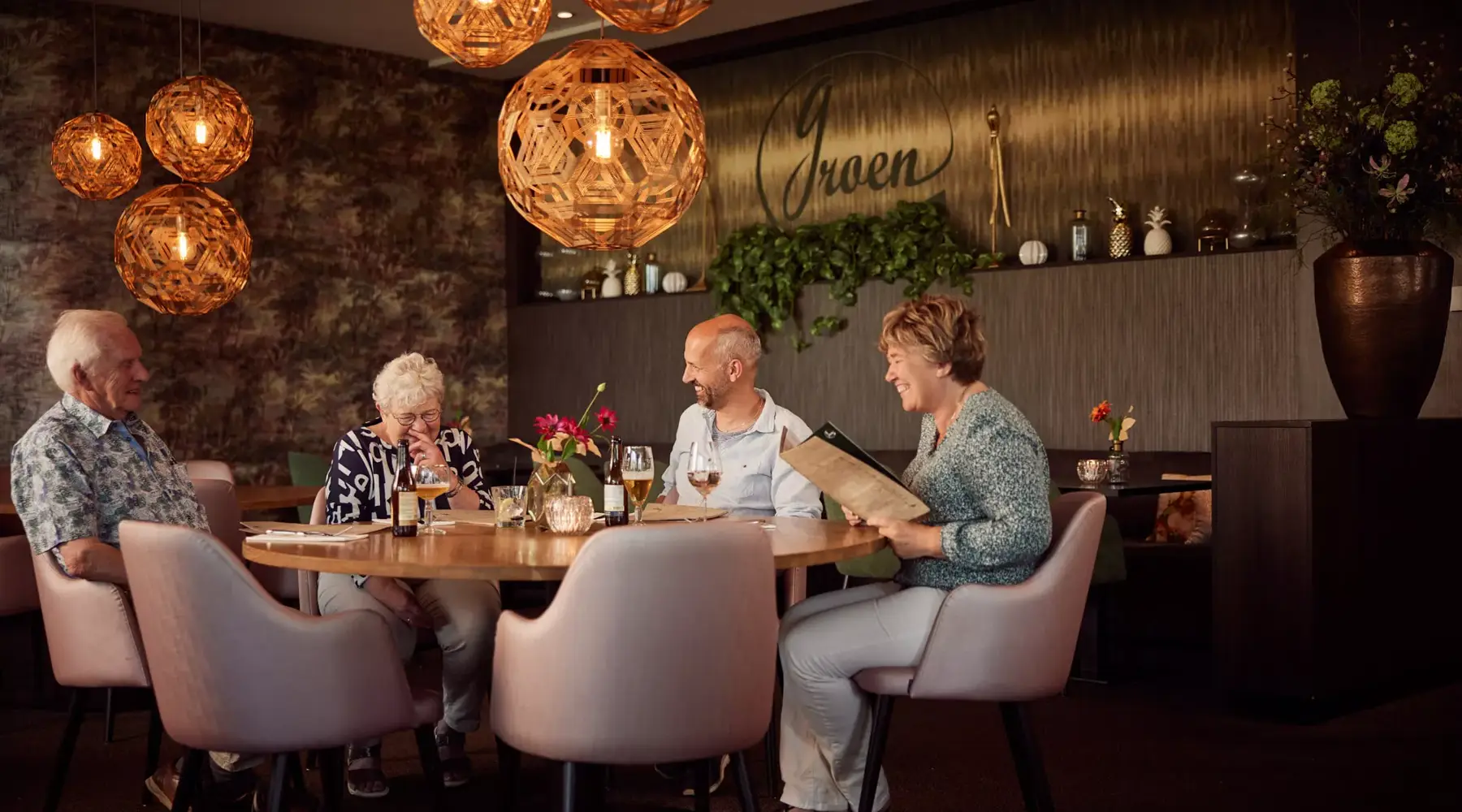 Een gepensioneerd koppel en een stel van middelbare leeftijd genieten samen van drankjes aan tafel.