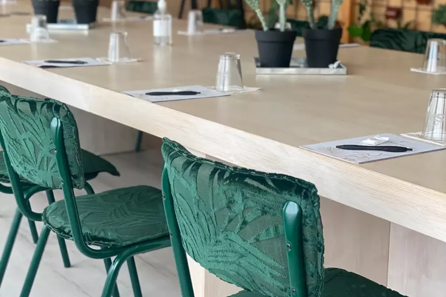 Een vergaderruimte met een lange houten tafel, groene stoelen, cactussen als decoratie en een plantenwand, in een natuurlijke sfeer.