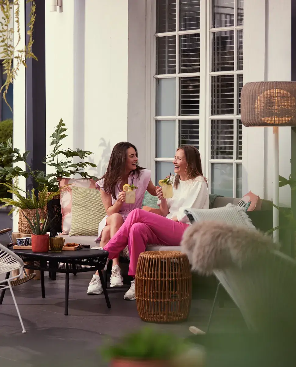 2 Frauen trinken ein Getränk auf der Terrasse. 