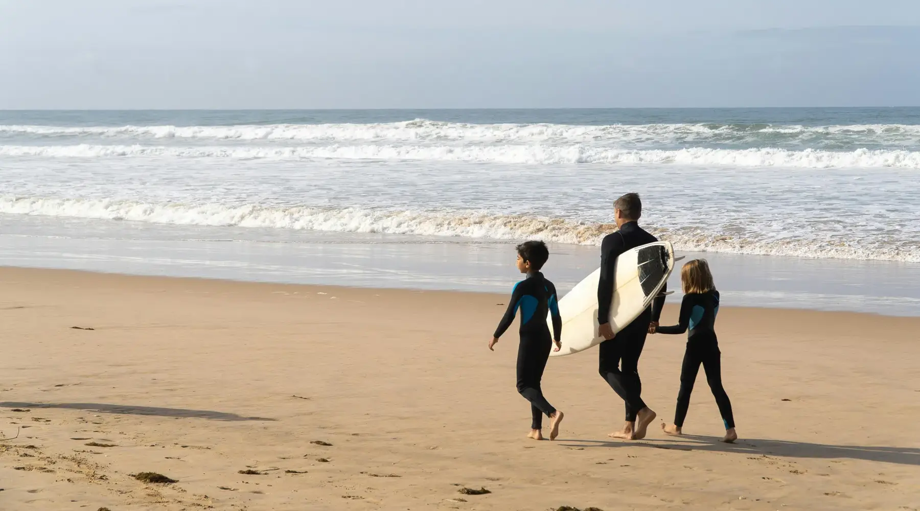 Father with surfboard and two children walking on the beach