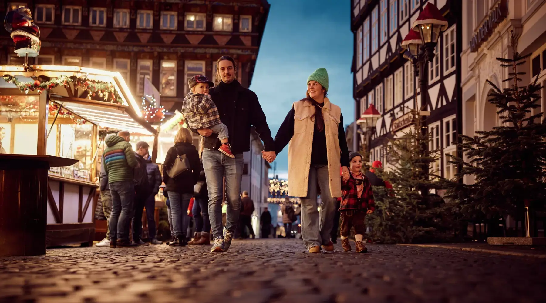 Eine Familie spaziert über eine gepflasterte Straße auf dem Weihnachtsmarkt in Hildesheim und genießt die festliche Atmosphäre und Dekorationen.