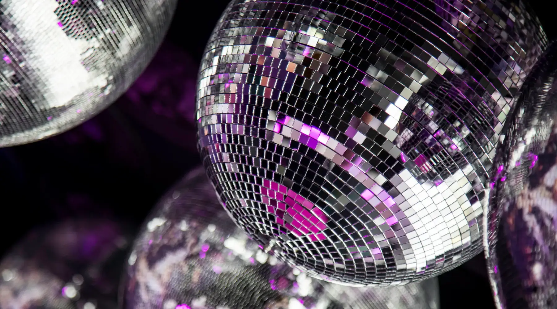 Nahaufnahme von glitzernden Discokugeln mit violetten Lichteffekten, passend zu einer festlichen Disco-Atmosphäre.