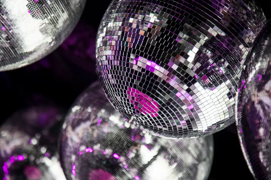 Close-up van glinsterende discoballen met paarse lichteffecten, passend bij een feestelijke disco-omgeving.