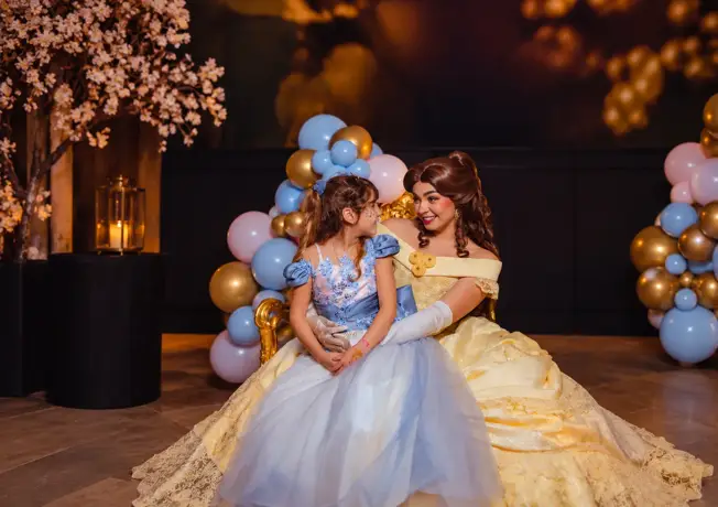 Prinses in gele jurk samen met een meisje in blauwe feestjurk tijdens een sprookjesachtig evenement.