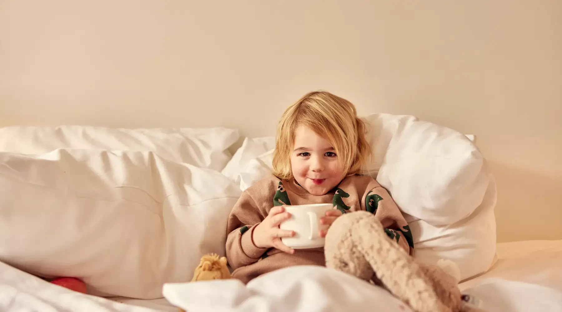 Kind zit op bed met een kop drinken