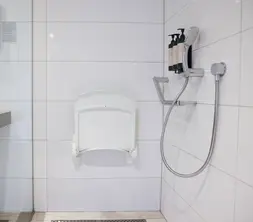 Barrierefreies Hotelbadezimmer mit ebenerdiger Dusche, Haltegriffen, klappbarem Duschsitz, Handbrause und Waschbecken.