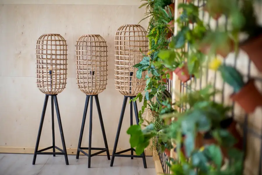 Drie houten lampen op zwarte standaards naast een groene plantenwand in een natuurlijke, moderne ruimte.
