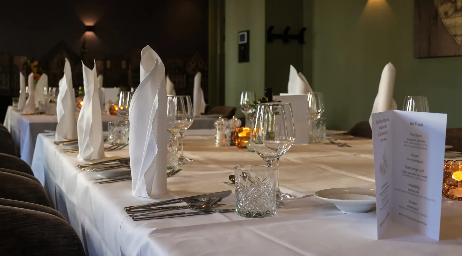 Festlich gedeckte lange Tafel mit weißen Stoffservietten, Gläsern und Besteck in einem Veranstaltungsraum des Van der Valk Hotels Hildesheim.