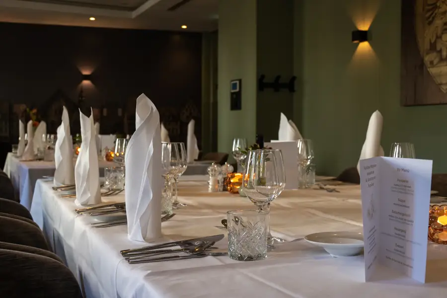 A festively set long table with white cloth napkins, glasses and cutlery in an event room of the Van der Valk Hotel Hildesheim.