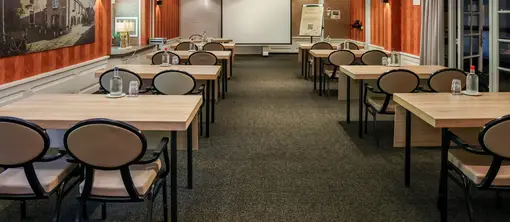 Salle de réunion De Uilenburg aménagée comme une salle de classe, avec lumière naturelle, murs à l'ambiance particulière et écran de présentation.