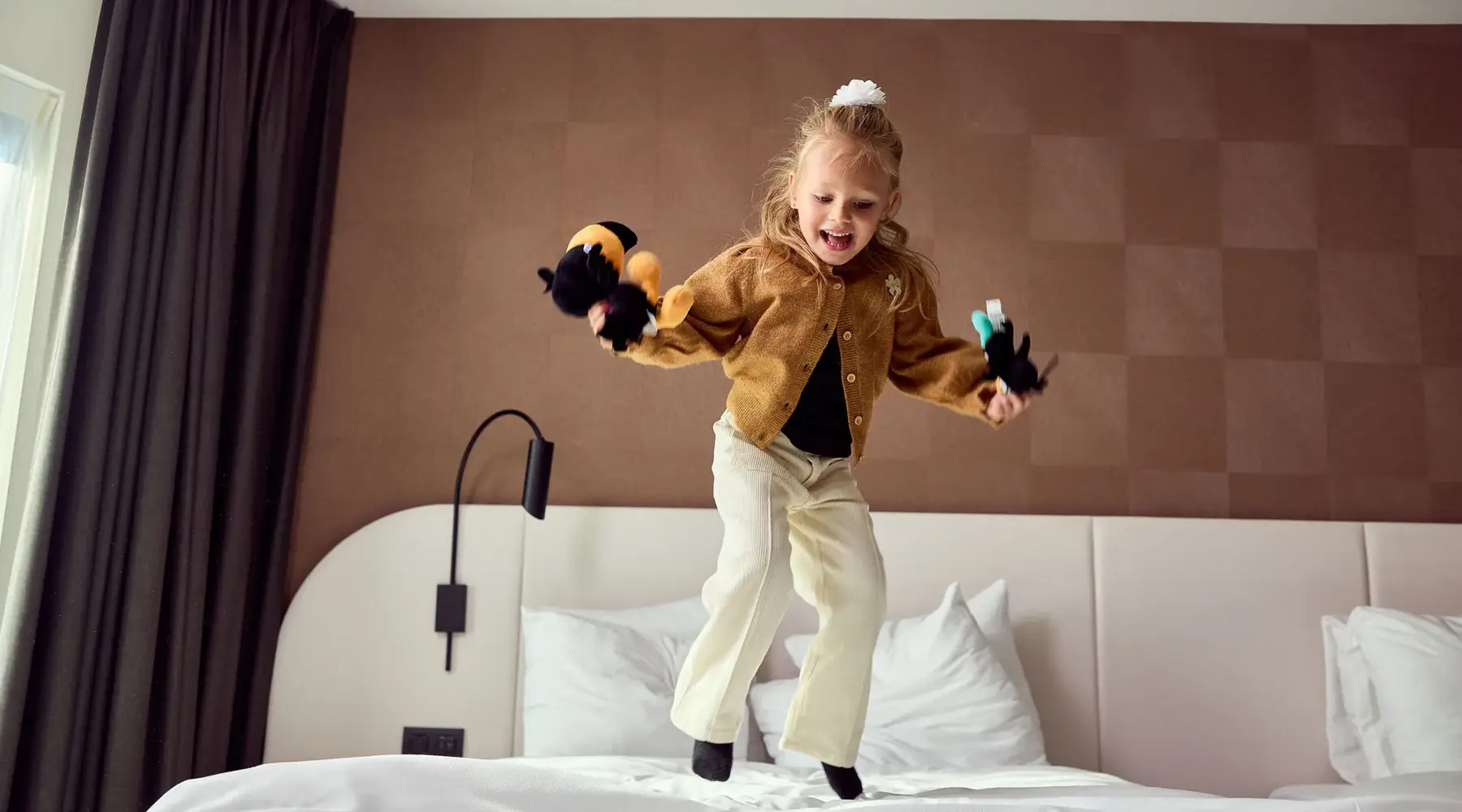 Meisje springt op bed met een Timo en Tiki Toekan knuffel.