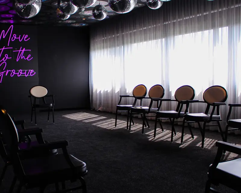 Een disco-vergaderruimte met discoballen aan het plafond, stoelen in een opstelling en veel lichtinval door de grote ramen.